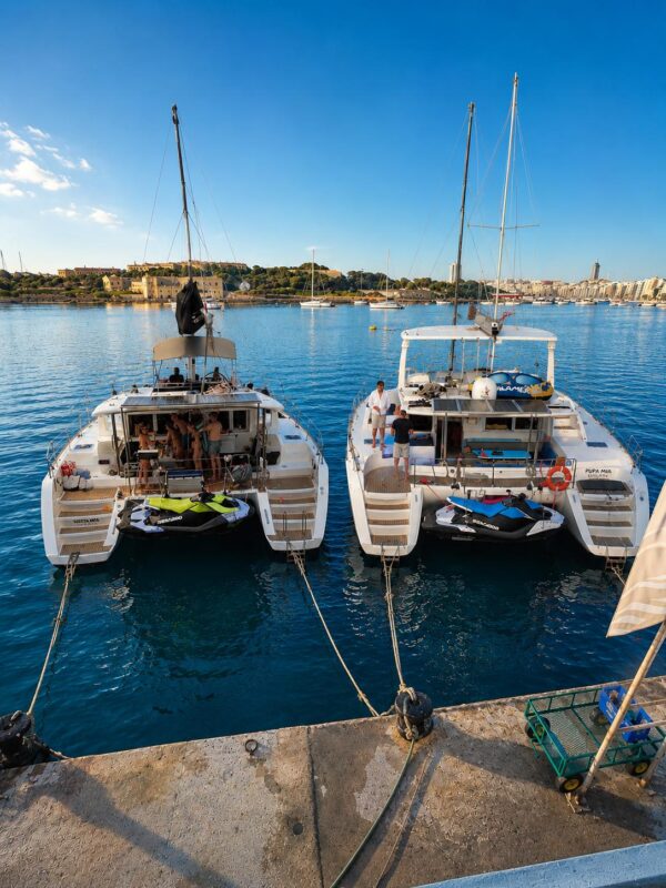 Siesta Mia and Pupa Mia catamarans moored with jet skis, Manoel Island and Sliema behind