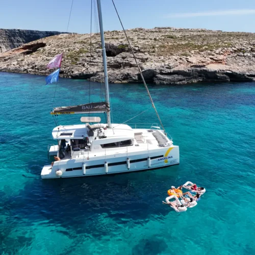 Angelina Mia Bali 4.0 catamaran anchored off Comino with guests relaxing on a floating mat