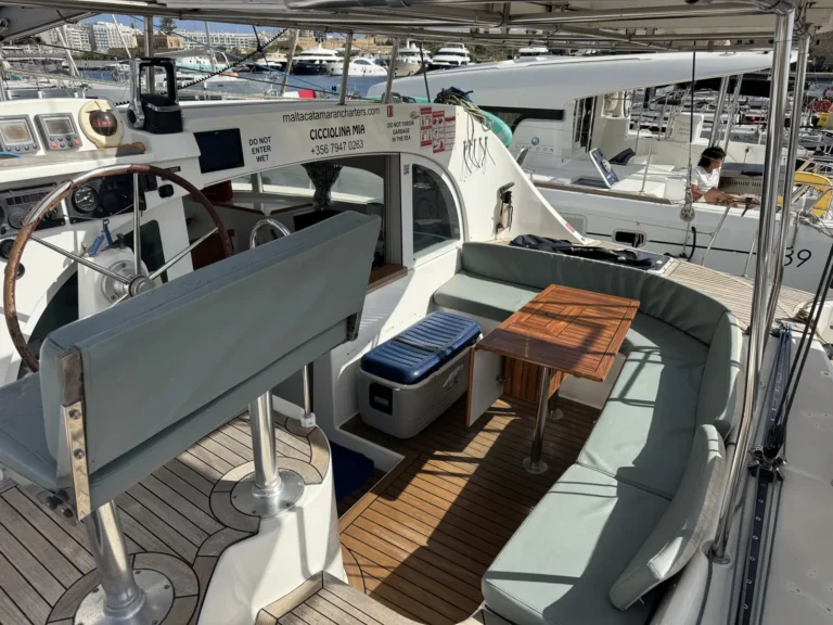 Shaded cockpit on Cicciolina Mia with cushioned seating, a teak table and a cooler box